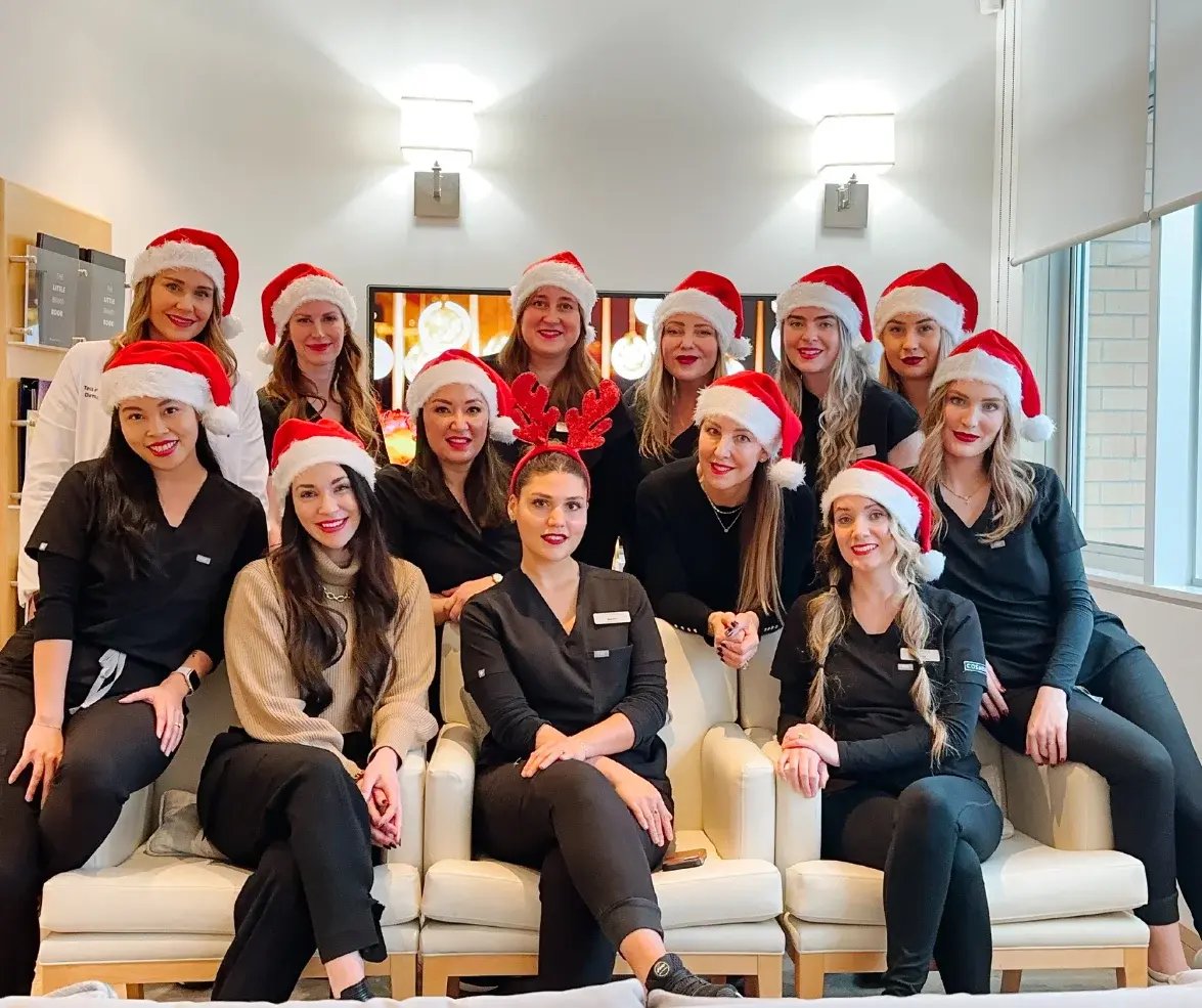 group-of-smiling-staff-wearing-santa-hats-and-reindeer-ears-sitting-together-in-clinic-celebrating-holiday-beauty-sale