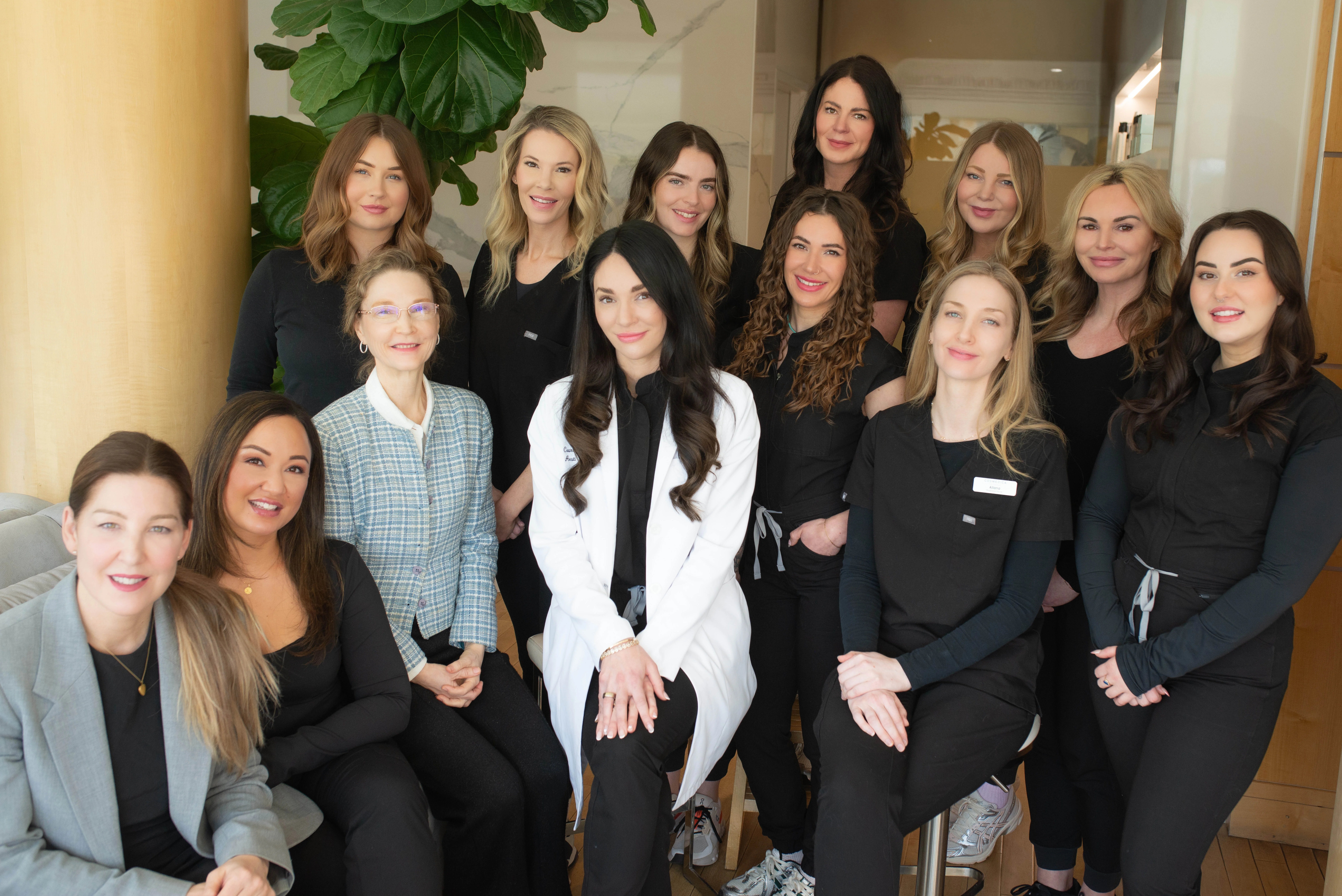 group-photo-of-aesthetic-clinic-team-with-women-smiling-and-wearing-black-and-gray-uniforms-in-a-bright-modern-office-setting