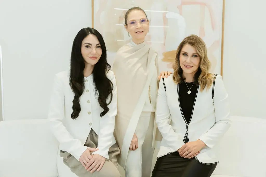 three-women-sitting-and-standing-on-white-sofa-in-bright-clinic-setting-wearing-light-colored-blazers